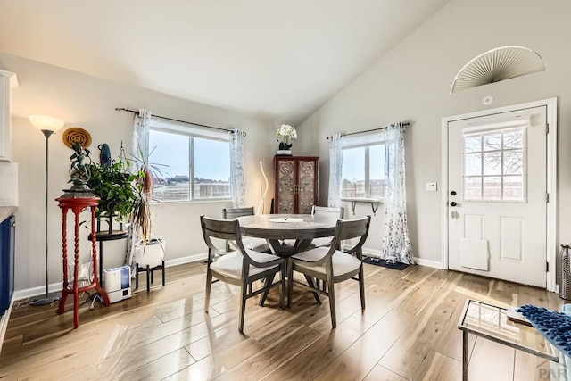 dining room with light wood-style floors, vaulted ceiling, and baseboards