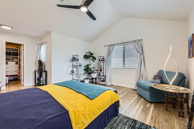 bedroom with lofted ceiling, a ceiling fan, baseboards, light wood-style floors, and a walk in closet