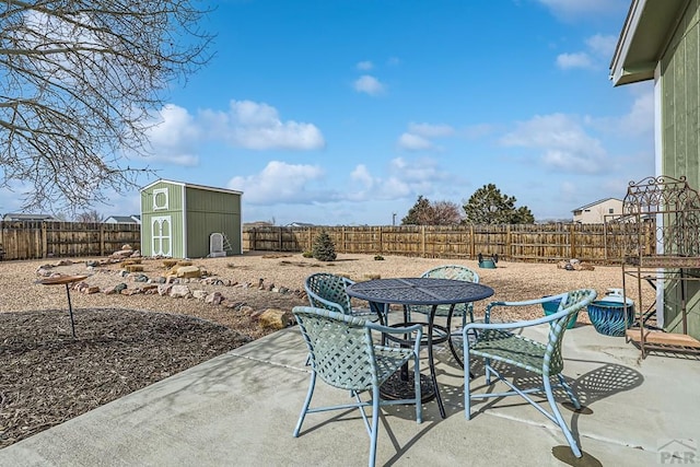 view of patio / terrace featuring a storage shed, a fenced backyard, outdoor dining area, and an outbuilding