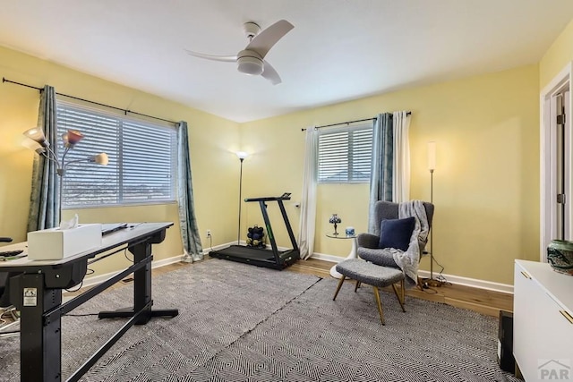 exercise room with a ceiling fan, baseboards, and wood finished floors