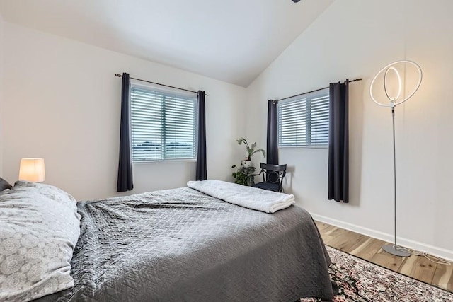 bedroom featuring lofted ceiling, multiple windows, baseboards, and wood finished floors