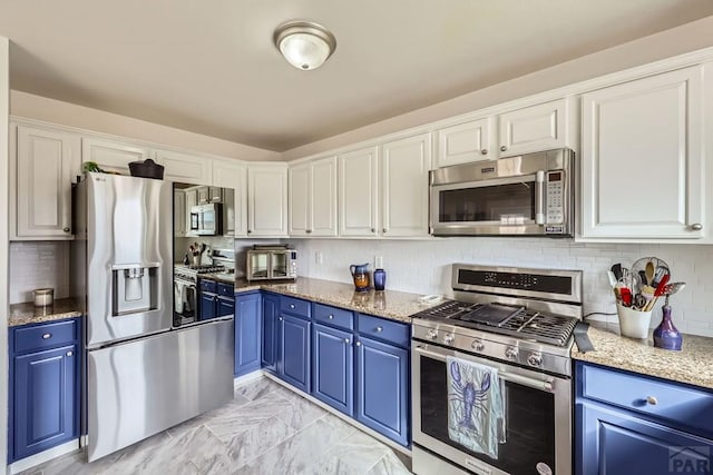 kitchen with stainless steel appliances, light stone counters, white cabinetry, and blue cabinets