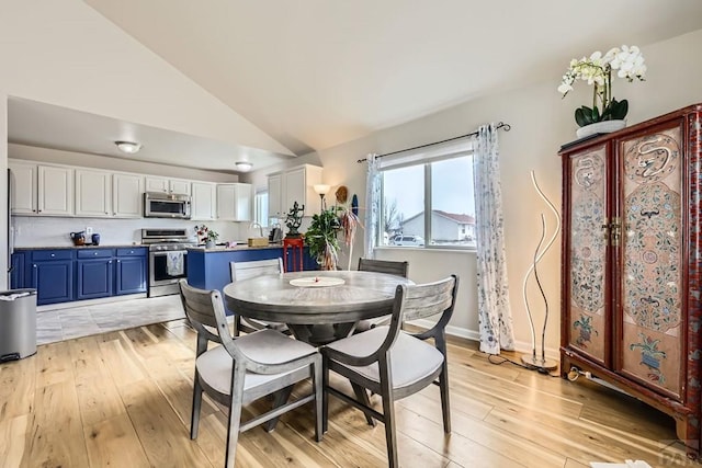 dining area with light wood-style floors, baseboards, and vaulted ceiling