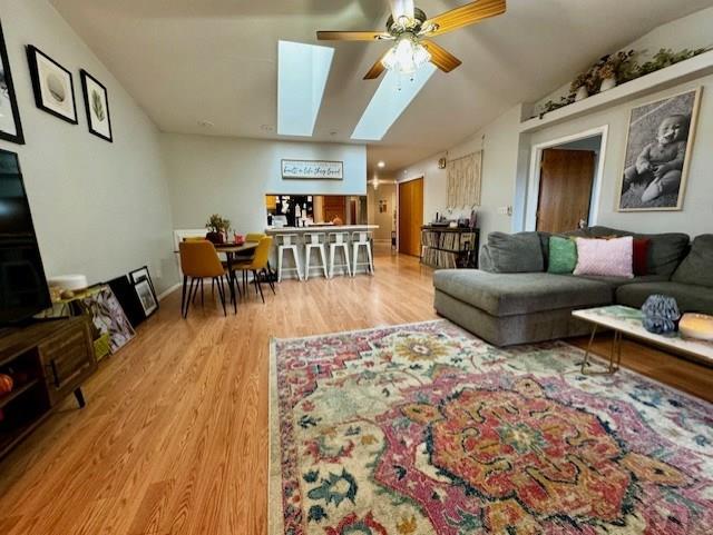 living area featuring a skylight, light wood finished floors, and a ceiling fan