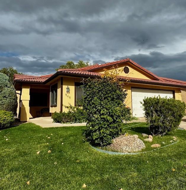 exterior space featuring an attached garage, a tile roof, a lawn, and stucco siding