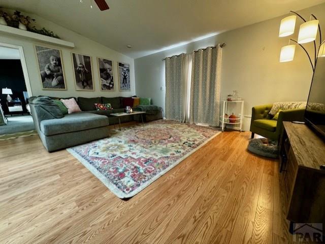 living room featuring a ceiling fan, vaulted ceiling, and light wood finished floors