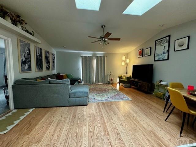 living area featuring lofted ceiling, light wood-type flooring, and a ceiling fan