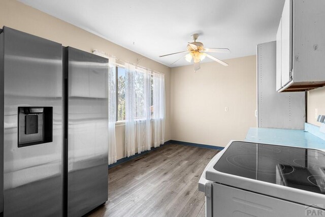 kitchen with stainless steel refrigerator with ice dispenser, white electric range oven, light countertops, light wood-style flooring, and white cabinetry