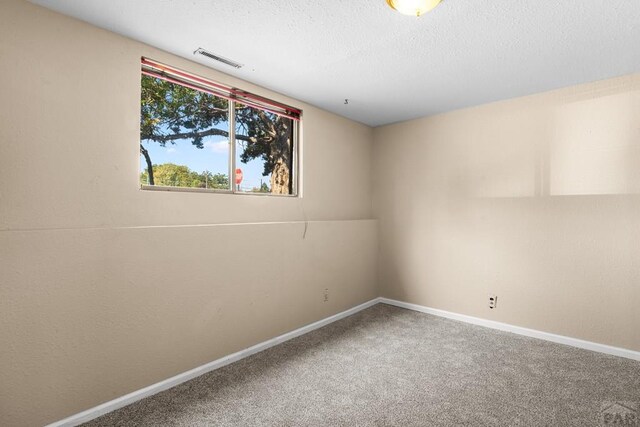 carpeted spare room with a textured ceiling, visible vents, and baseboards