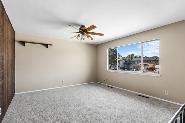 carpeted spare room featuring ceiling fan, visible vents, and baseboards