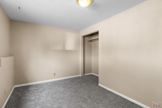 unfurnished bedroom with a textured ceiling, baseboards, dark colored carpet, and a closet