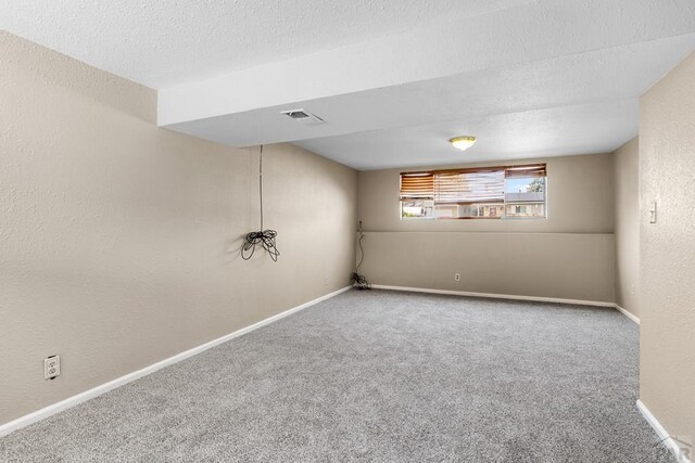 basement with carpet floors, visible vents, a textured ceiling, and baseboards