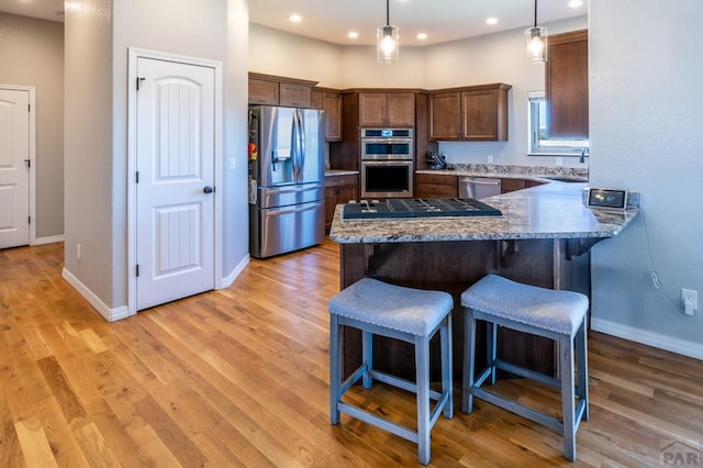 1557 28th Ln, Pueblo, CO 81006 - kitchen featuring stainless steel appliances, a peninsula, a kitchen bar, light wood finished floors, and recessed lighting