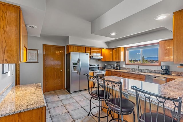 kitchen with a breakfast bar, brown cabinets, appliances with stainless steel finishes, a sink, and under cabinet range hood