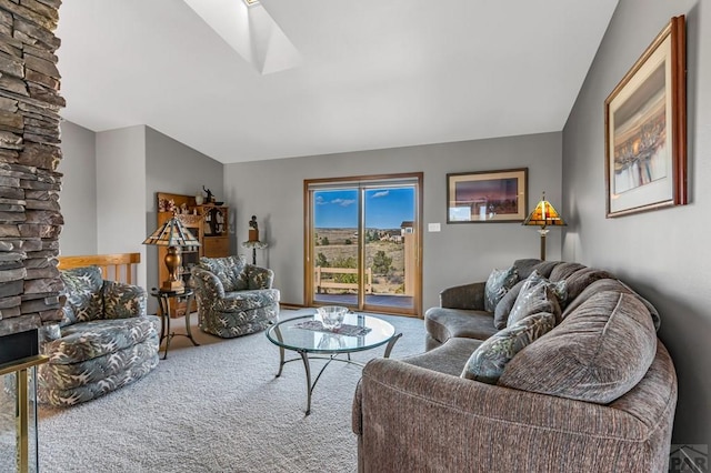 carpeted living room with vaulted ceiling with skylight and a stone fireplace