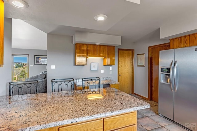 kitchen featuring light stone counters, brown cabinets, and stainless steel fridge with ice dispenser