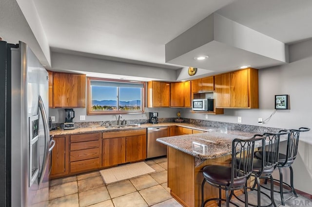 kitchen featuring appliances with stainless steel finishes, brown cabinets, a breakfast bar area, a peninsula, and a sink