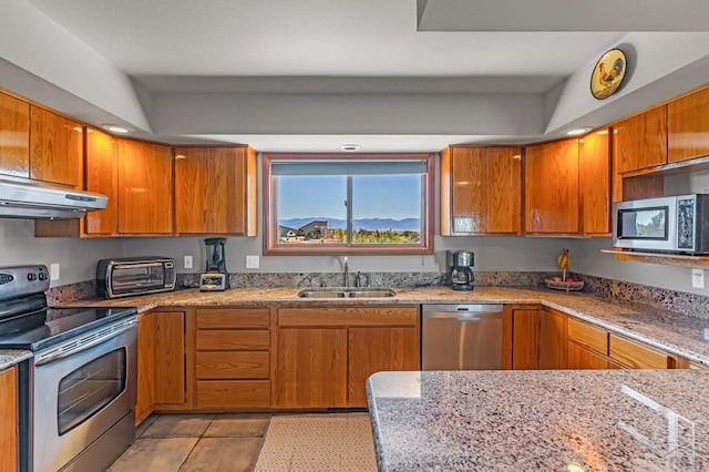 kitchen featuring brown cabinets, appliances with stainless steel finishes, a sink, and under cabinet range hood