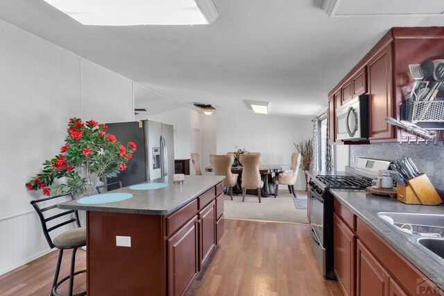 kitchen with a breakfast bar area, wood finished floors, a center island, stainless steel appliances, and a sink