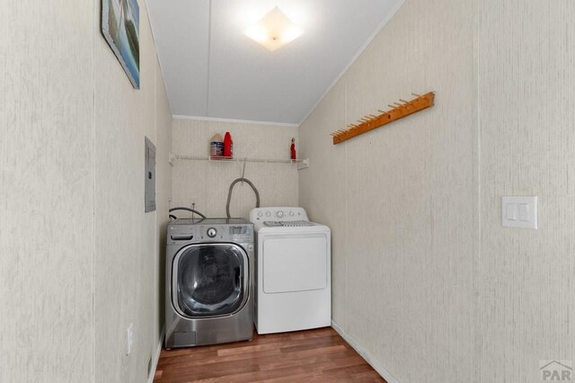 clothes washing area featuring crown molding, washing machine and clothes dryer, wood finished floors, laundry area, and electric panel