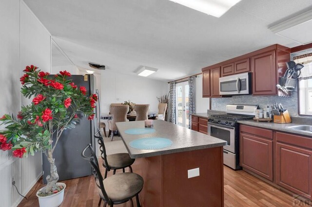 kitchen with stainless steel appliances, a kitchen island, a kitchen breakfast bar, light wood finished floors, and dark countertops