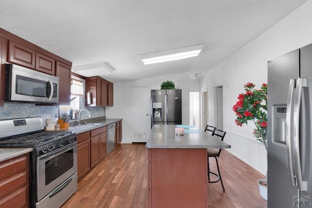 kitchen featuring a center island, stainless steel appliances, a sink, light wood-type flooring, and a kitchen bar