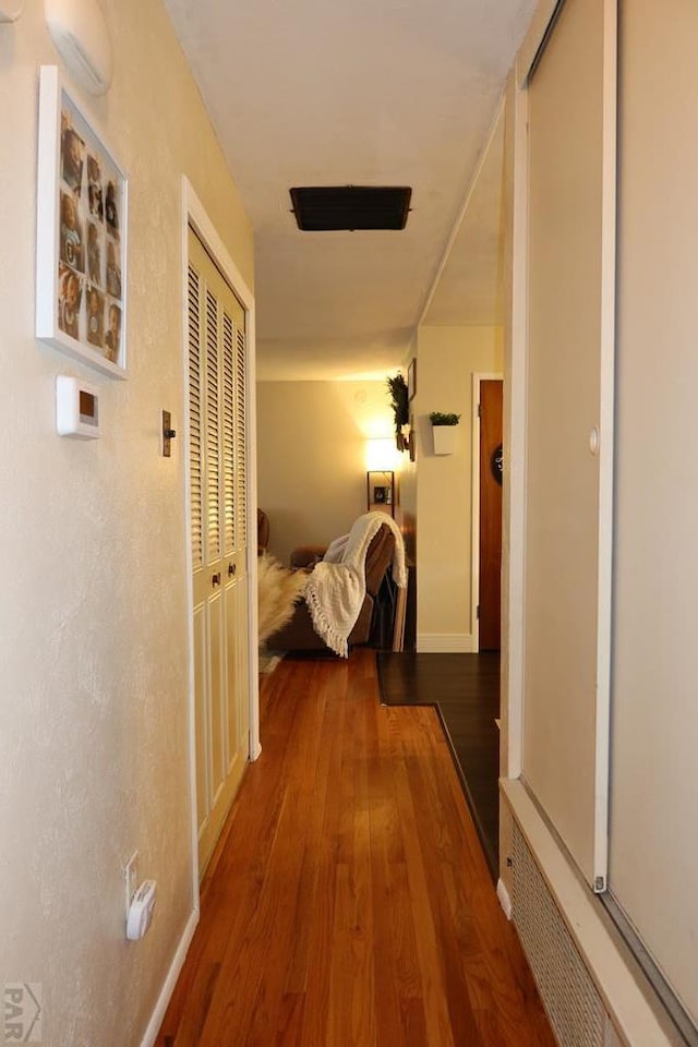 hallway with baseboards, visible vents, and wood finished floors