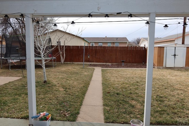 view of yard with a trampoline, a fenced backyard, an outdoor structure, and a storage unit