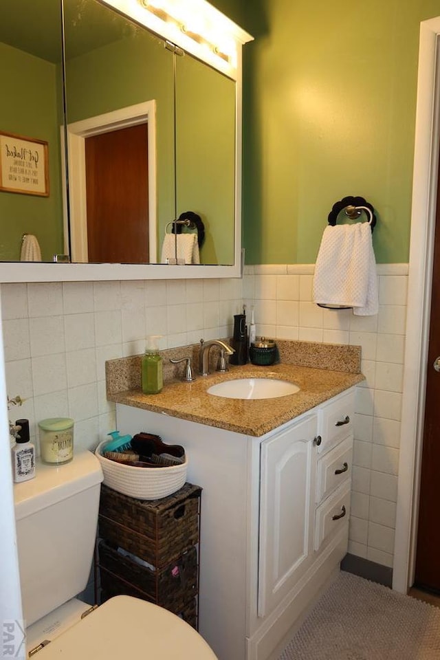 half bath with toilet, a wainscoted wall, tile walls, and vanity