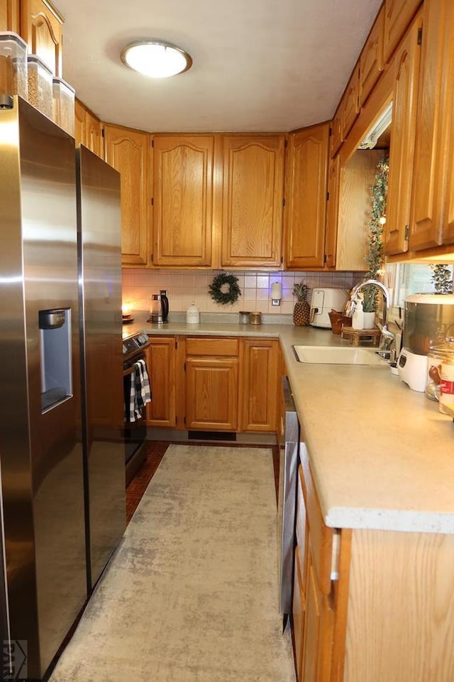 kitchen with stove, a sink, stainless steel fridge with ice dispenser, light countertops, and decorative backsplash