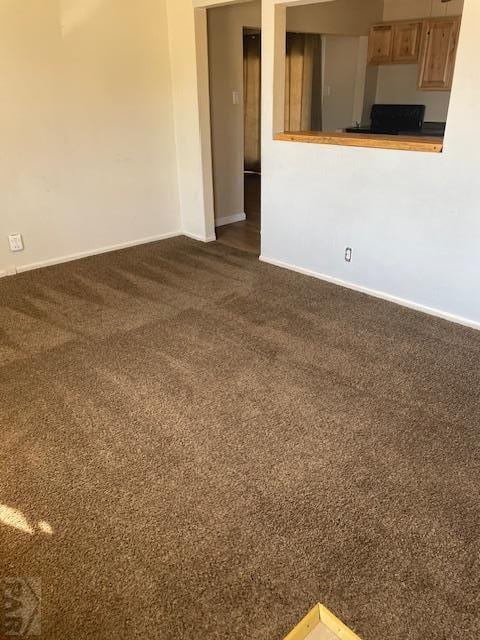 unfurnished living room featuring dark carpet and baseboards