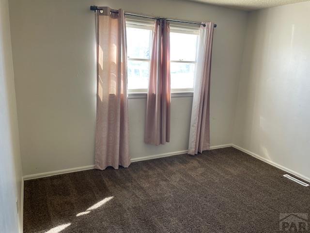 unfurnished room with a textured ceiling, dark colored carpet, visible vents, and baseboards