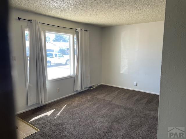 spare room with baseboards, dark carpet, and a textured ceiling