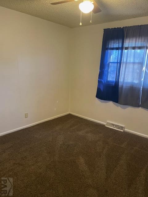 empty room with dark colored carpet, visible vents, a ceiling fan, a textured ceiling, and baseboards