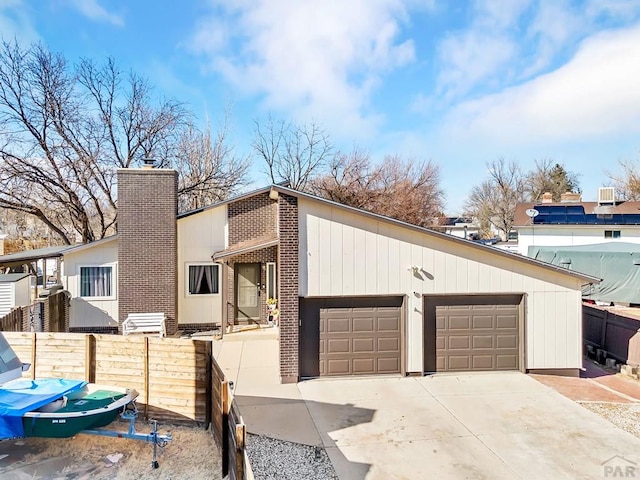 mid-century home featuring brick siding, a chimney, a detached garage, and fence