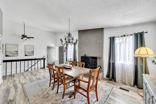 dining area with light wood finished floors, visible vents, ceiling fan with notable chandelier, and a textured ceiling