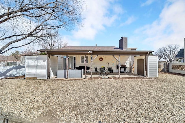 back of property with fence, a chimney, a storage shed, a patio area, and an outbuilding