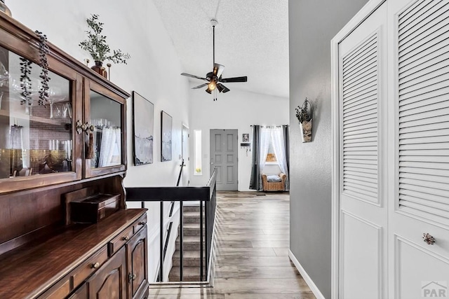 hall with baseboards, lofted ceiling, a textured ceiling, and light wood finished floors