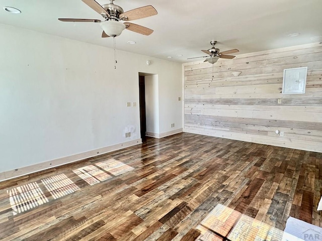 empty room featuring a ceiling fan, wooden walls, wood finished floors, electric panel, and baseboards