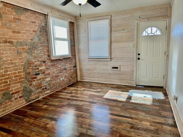 foyer featuring ceiling fan, brick wall, dark wood-type flooring, and wood walls