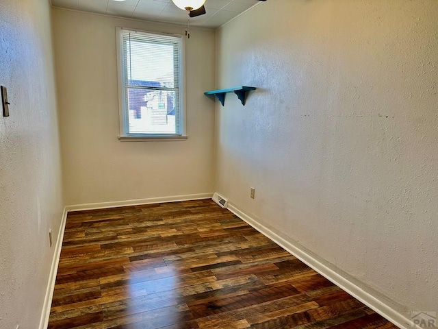 spare room with dark wood-type flooring, a textured wall, and baseboards