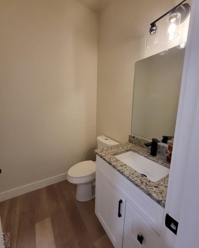 half bath featuring toilet, baseboards, wood finished floors, and vanity