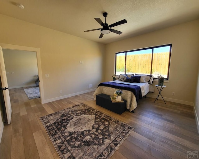 bedroom with a ceiling fan, a textured ceiling, baseboards, and wood finished floors