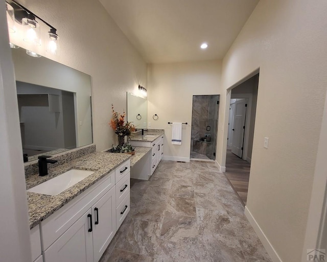 full bath featuring two vanities, baseboards, a walk in shower, and a sink