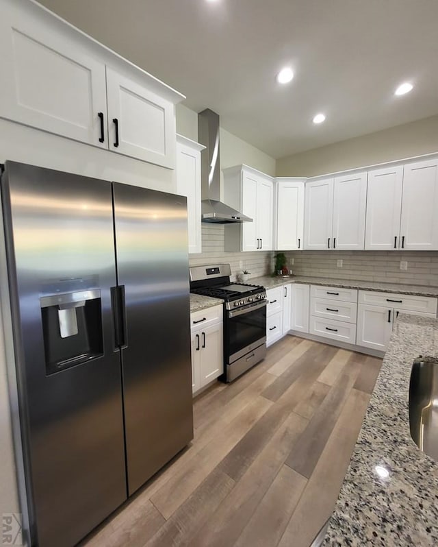 kitchen featuring wall chimney range hood, white cabinetry, appliances with stainless steel finishes, and light stone counters