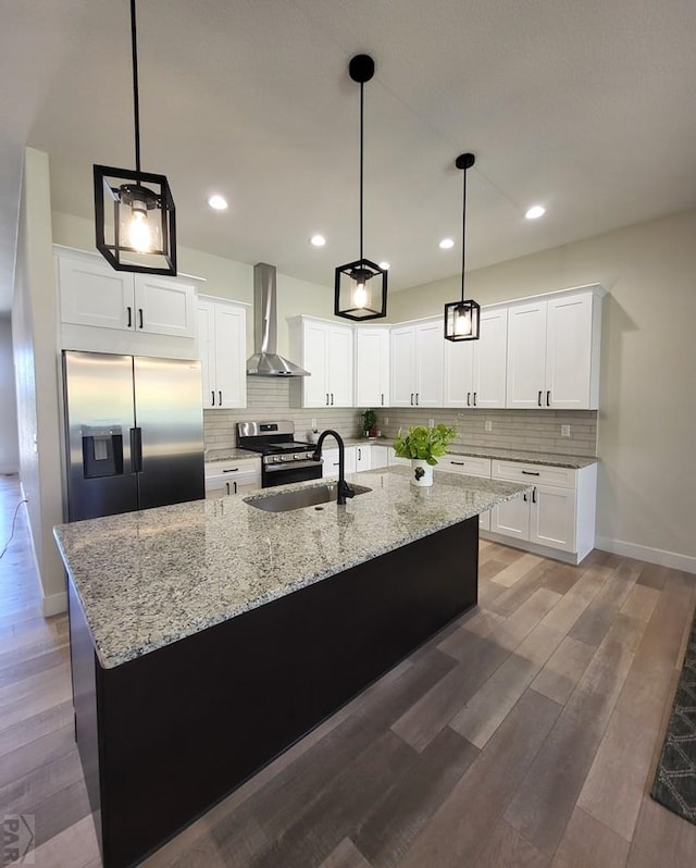 kitchen with a center island with sink, appliances with stainless steel finishes, white cabinets, a sink, and wall chimney exhaust hood