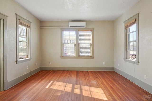 empty room with a wealth of natural light, a wall unit AC, and wood finished floors