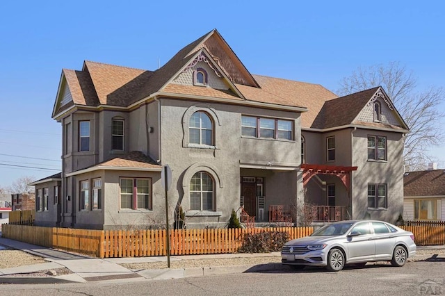 view of front of home featuring a shingled roof, a fenced front yard, and stucco siding