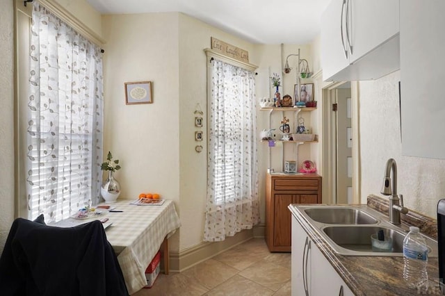 kitchen with light tile patterned floors, baseboards, white cabinetry, and a sink