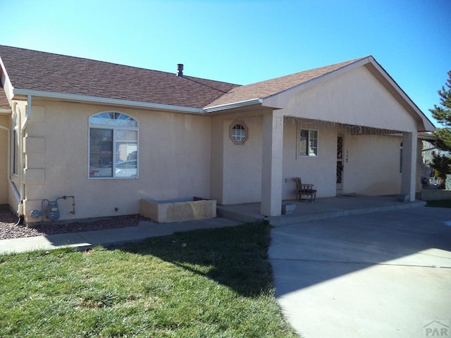 ranch-style home with roof with shingles, a front yard, concrete driveway, and stucco siding